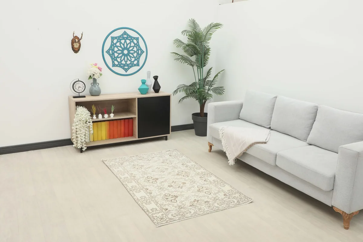 Ivory and tan rug placed in a room setting with a sofa and cabinet, showing its scale.