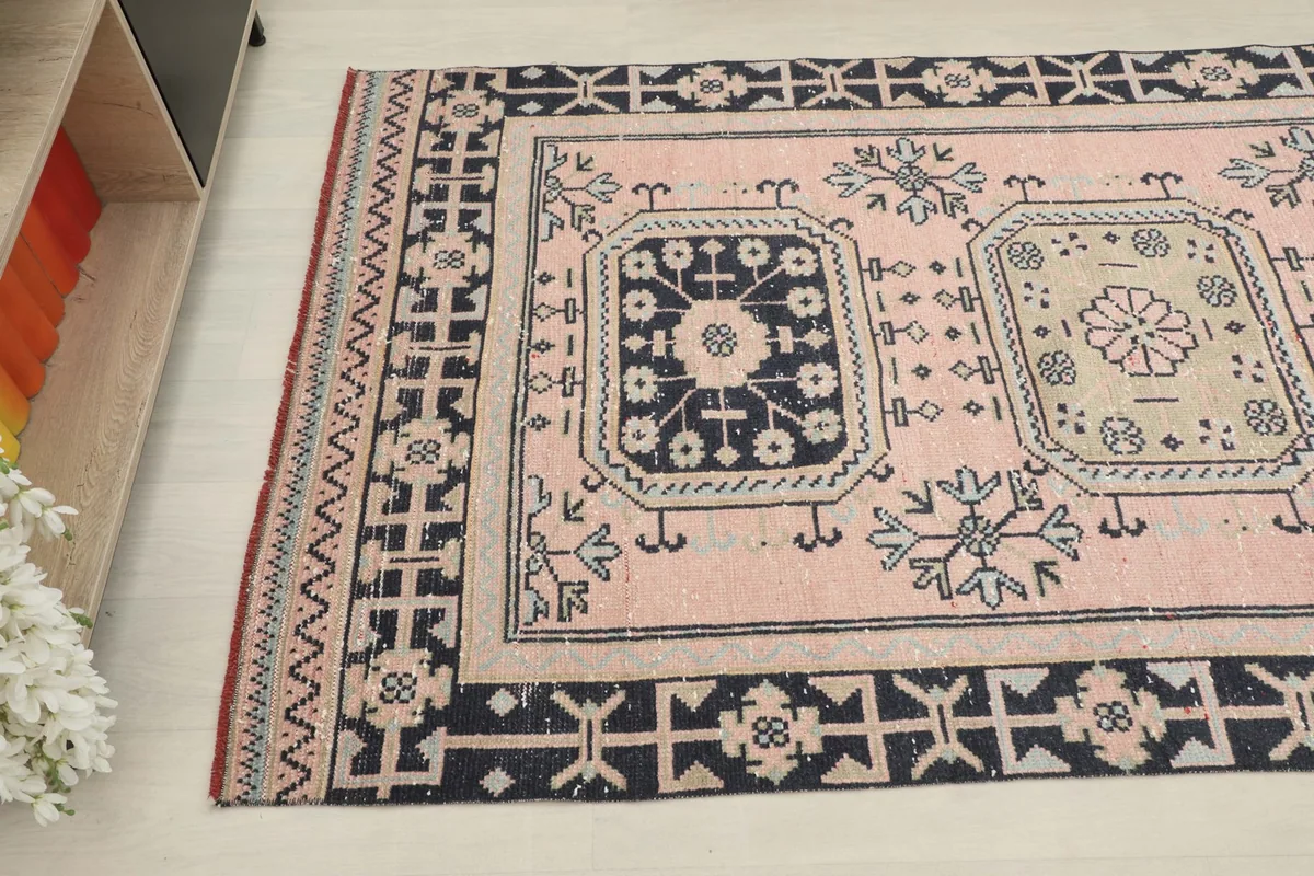 Angled view of the rug's side, showing the pink field and navy border with tribal details
