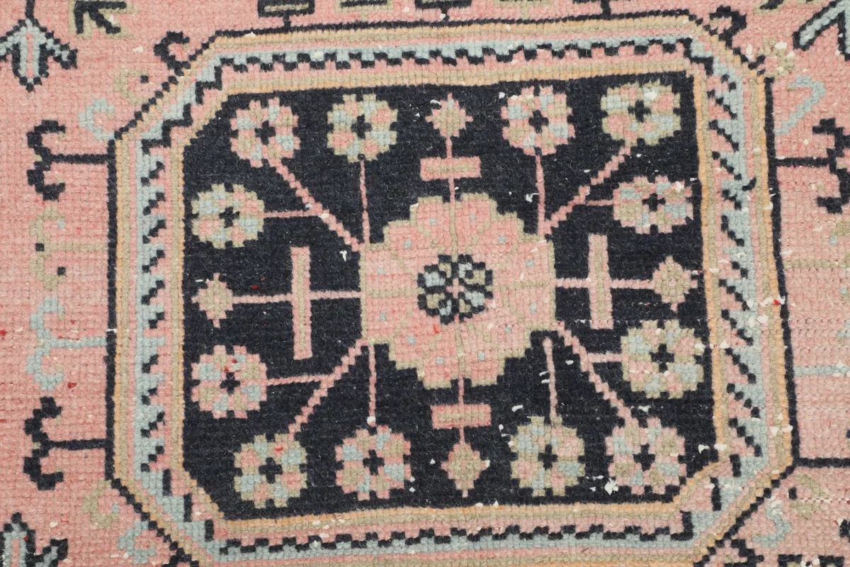 Close-up of a navy geometric medallion on the pink field, showing individual knot work
