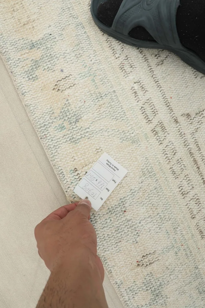 Hand holding a tag near the rug's border, showing the texture and pattern