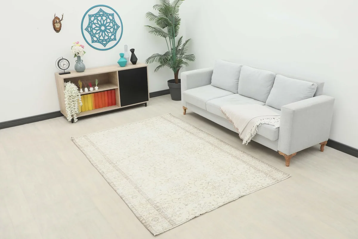 Ivory and beige vintage rug displayed in a bright room setting with a light gray sofa and modern decor.