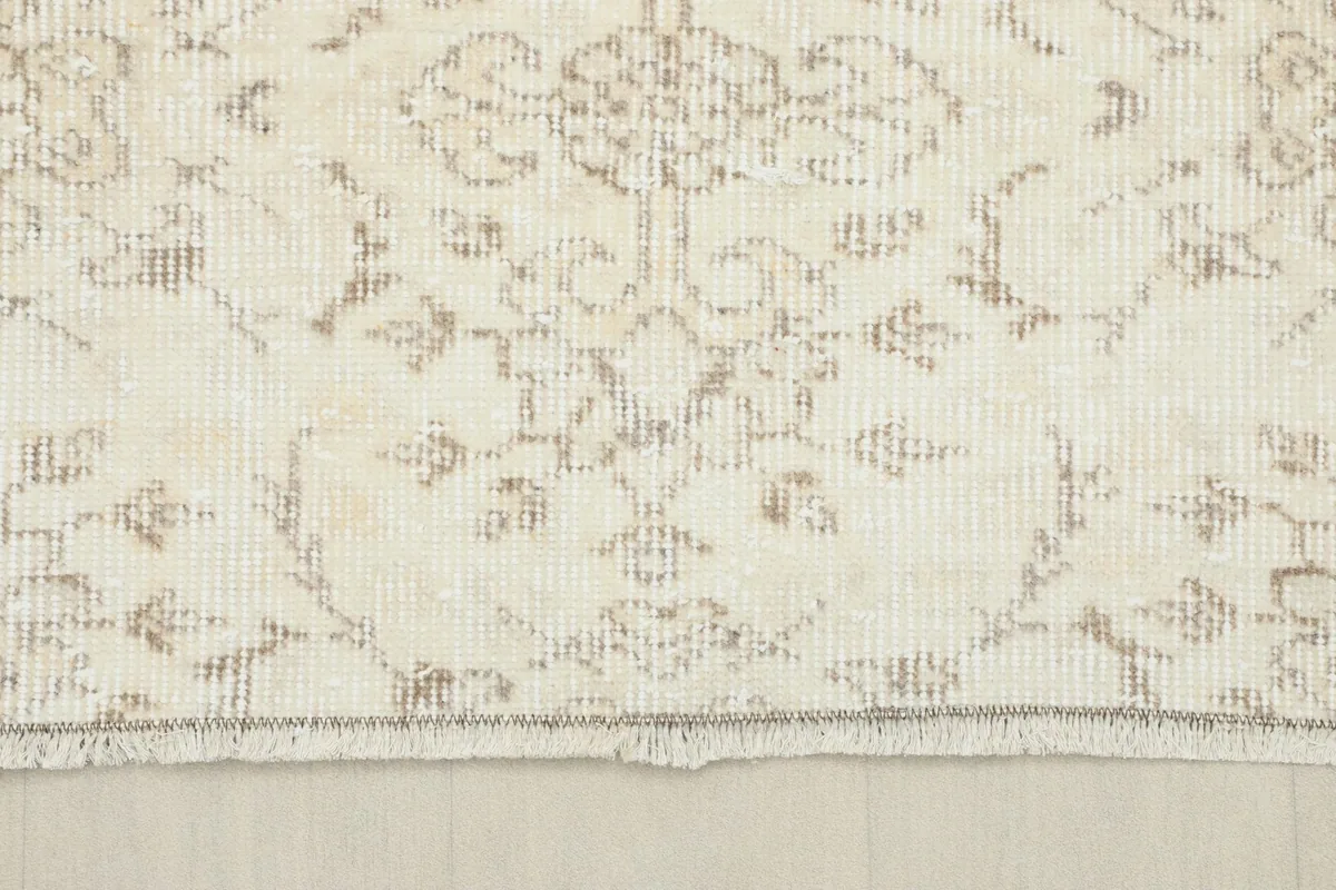Close-up of the short, natural fringe and edge of the vintage ivory and beige wool rug.