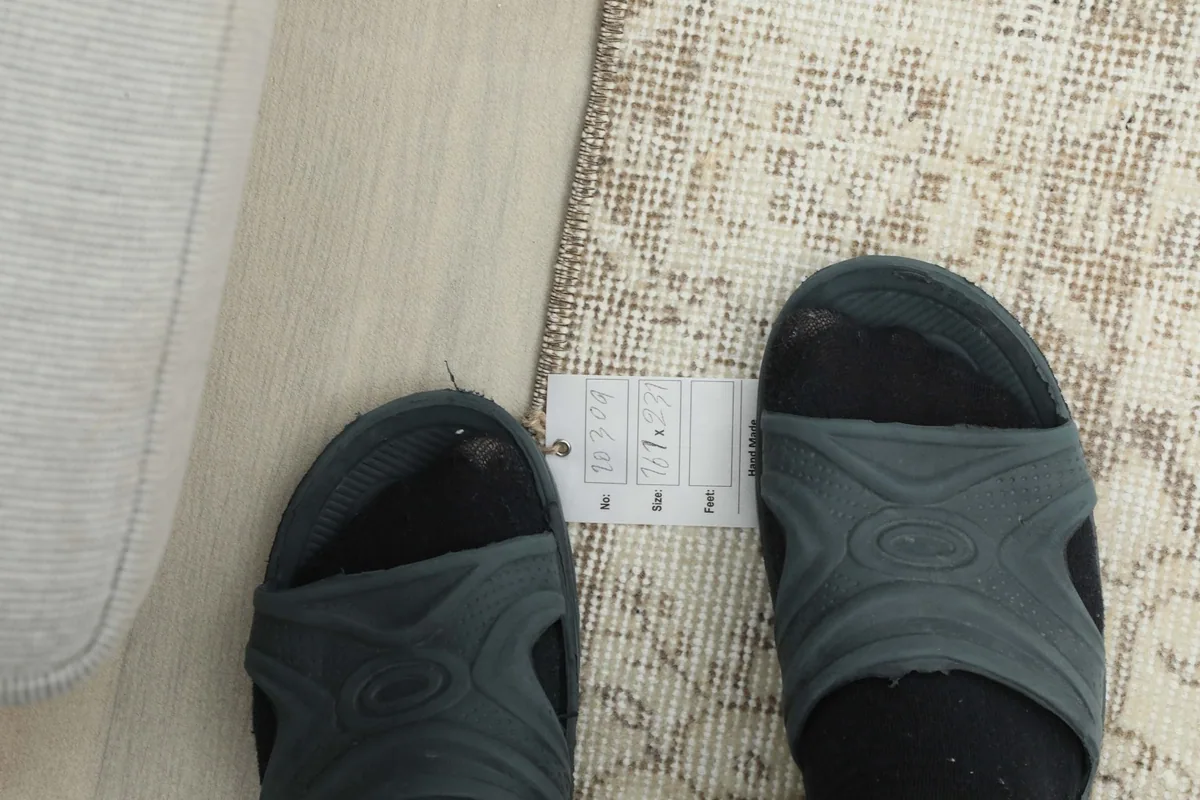 Feet in sandals next to a size label on the rug, providing a scale reference for the pile height.