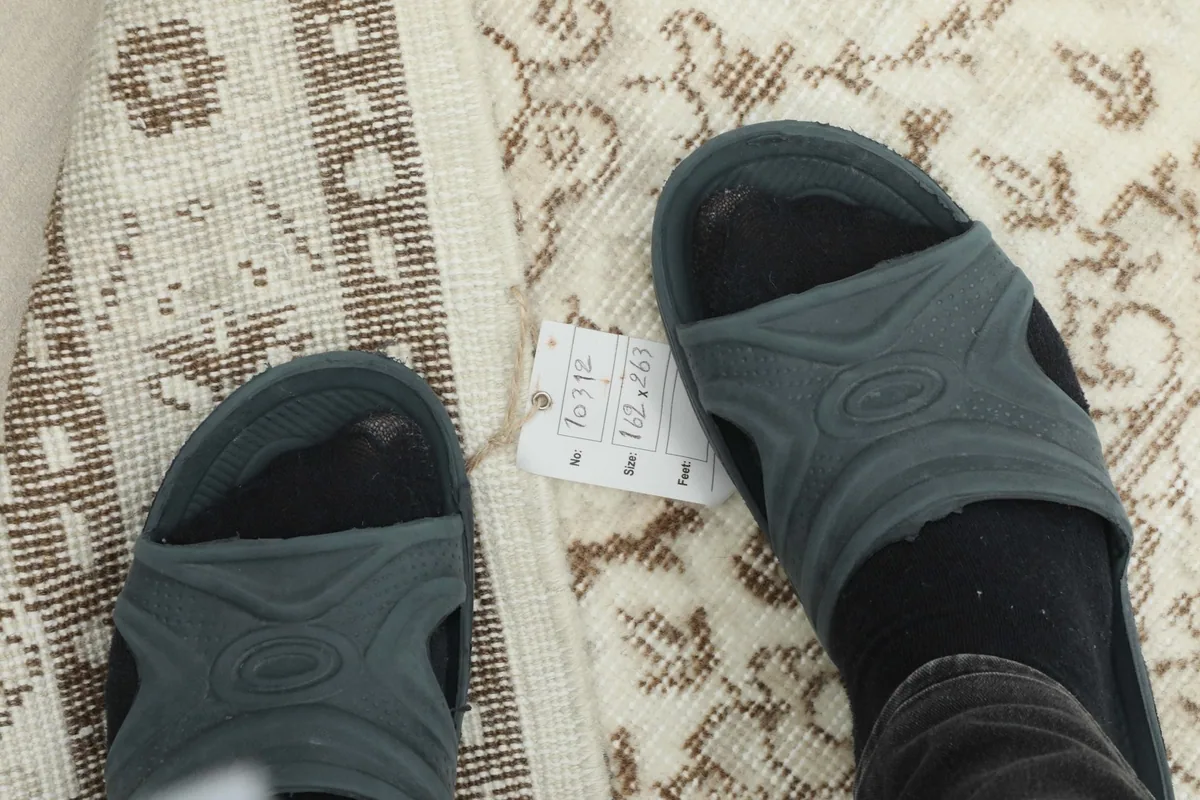 Feet in sandals on the rug, indicating its size and scale, with a tag visible