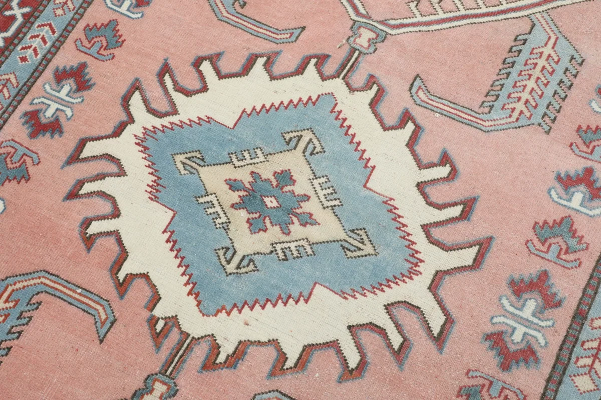 Close-up detail of the central blue and ivory tribal medallion motif on the rose field