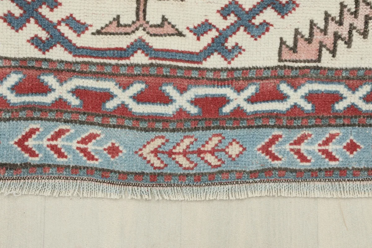 Detail of the rug's short fringe and the blue and red geometric patterns of the outer border