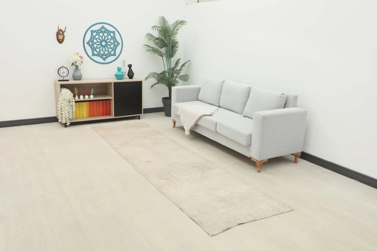Beige runner rug laid out in a modern room setting with a light gray sofa and wooden cabinet.