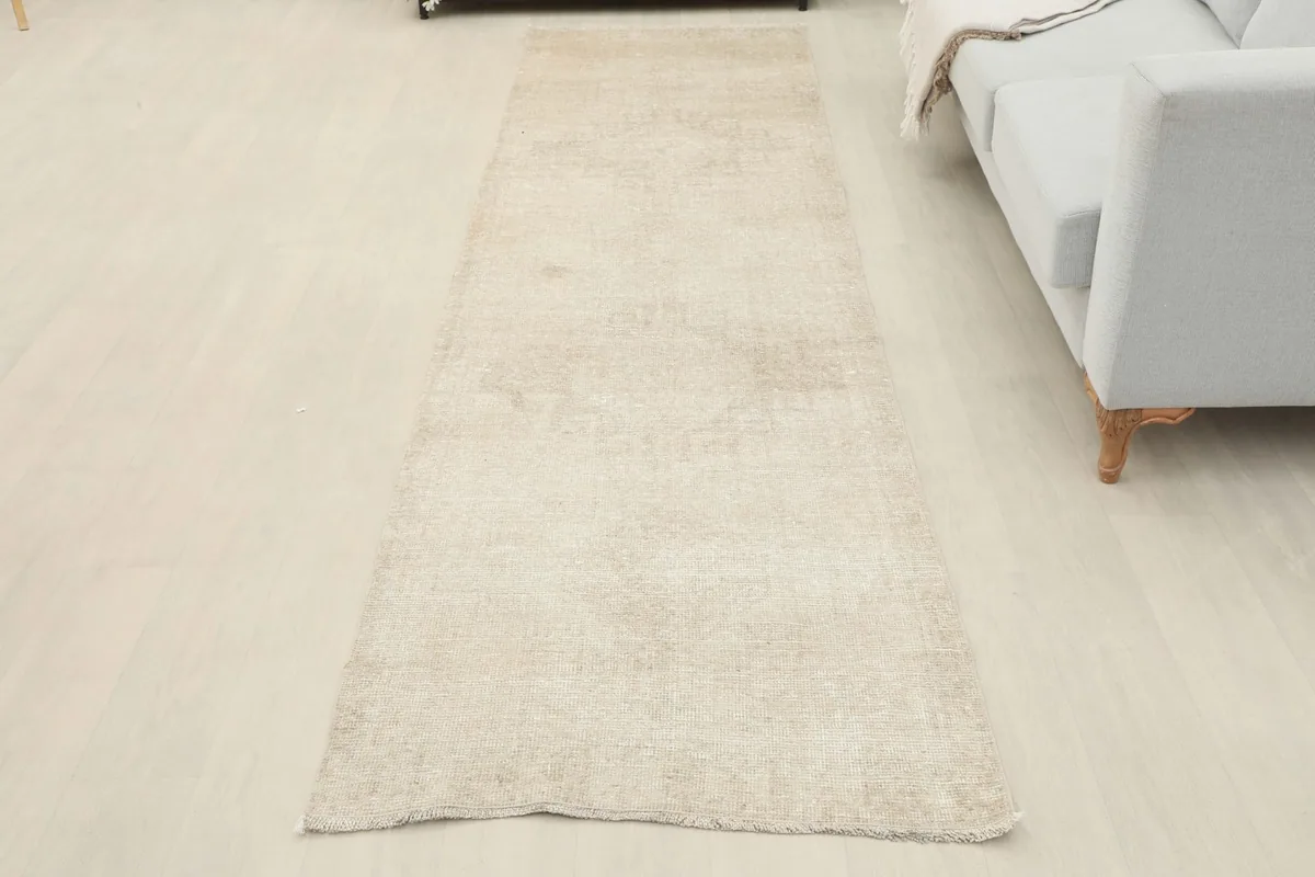 Full overhead view of the beige runner rug laid out on a light-colored floor in a room, showing its complete length.
