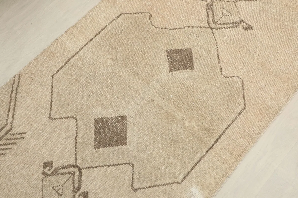 Close-up on a central brown geometric motif against the beige background, showing wear.