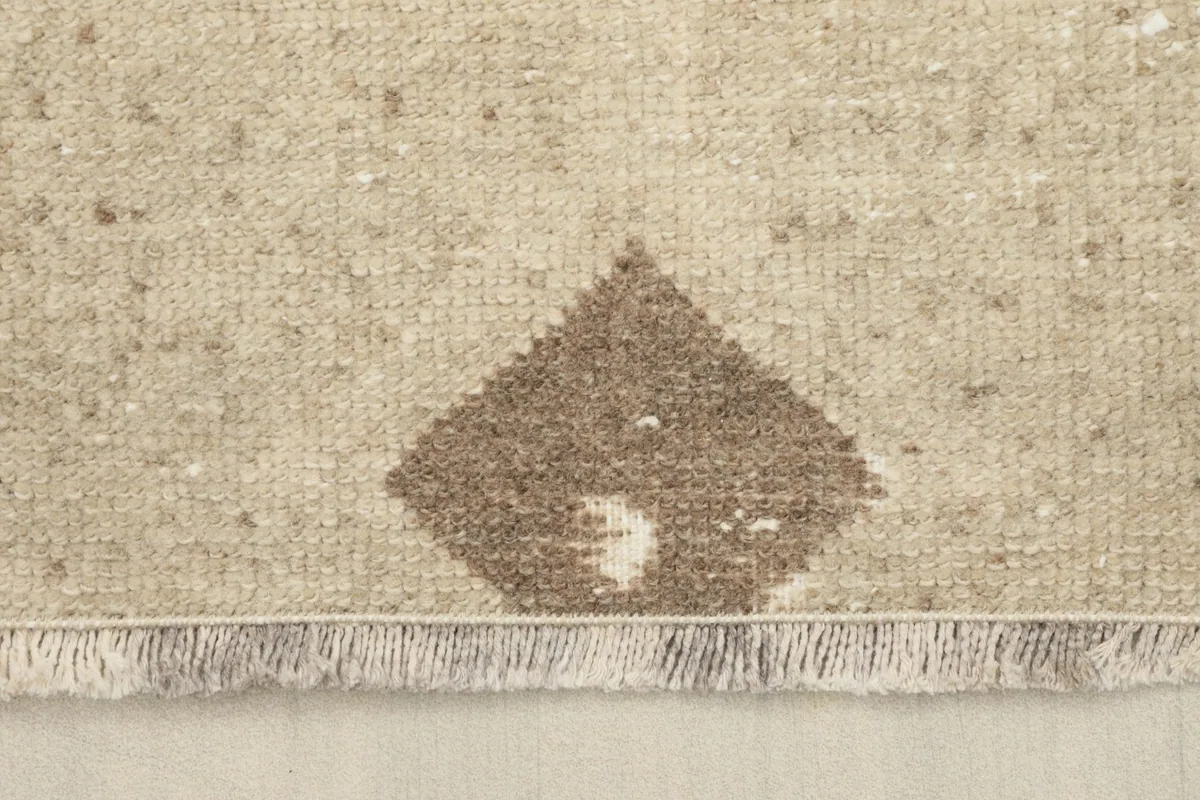 End of the runner rug showing the short, natural wool fringes and a brown diamond motif.