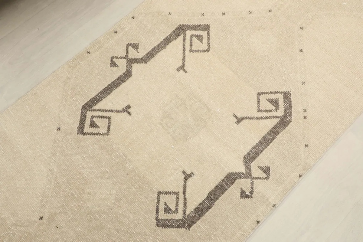 Angled close-up of a central gray tribal motif on the ivory background of the vintage runner rug.