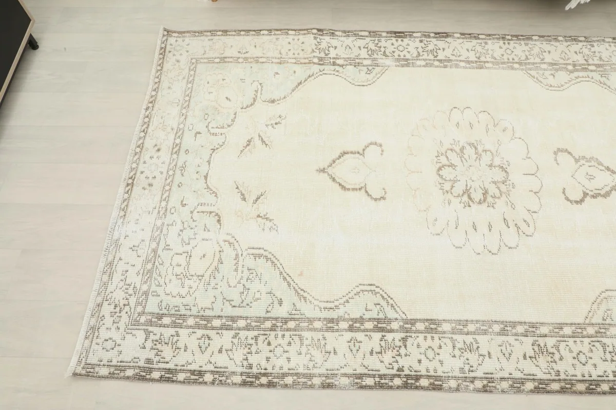 Overhead angled shot of the rug, highlighting the faded gray and tan motifs on the ivory background.