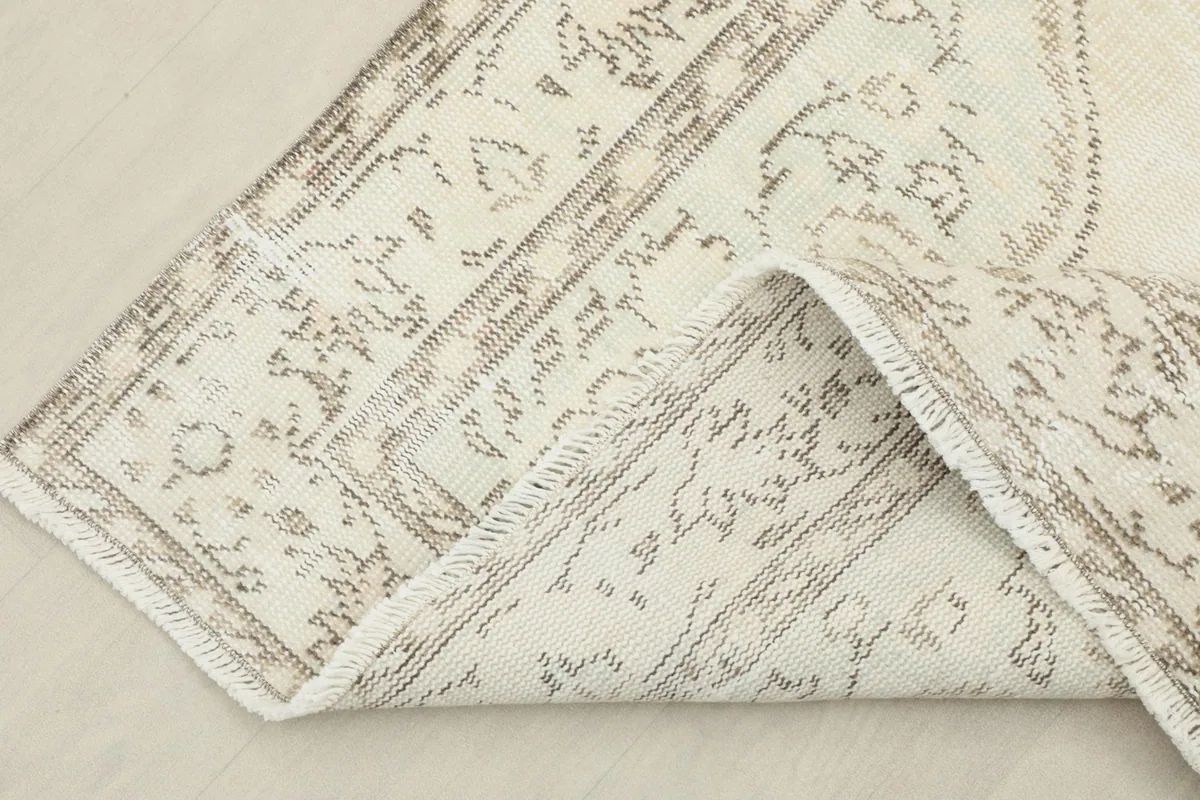 Corner of the rug folded back, showing the cotton foundation and the reverse side of the knotting.