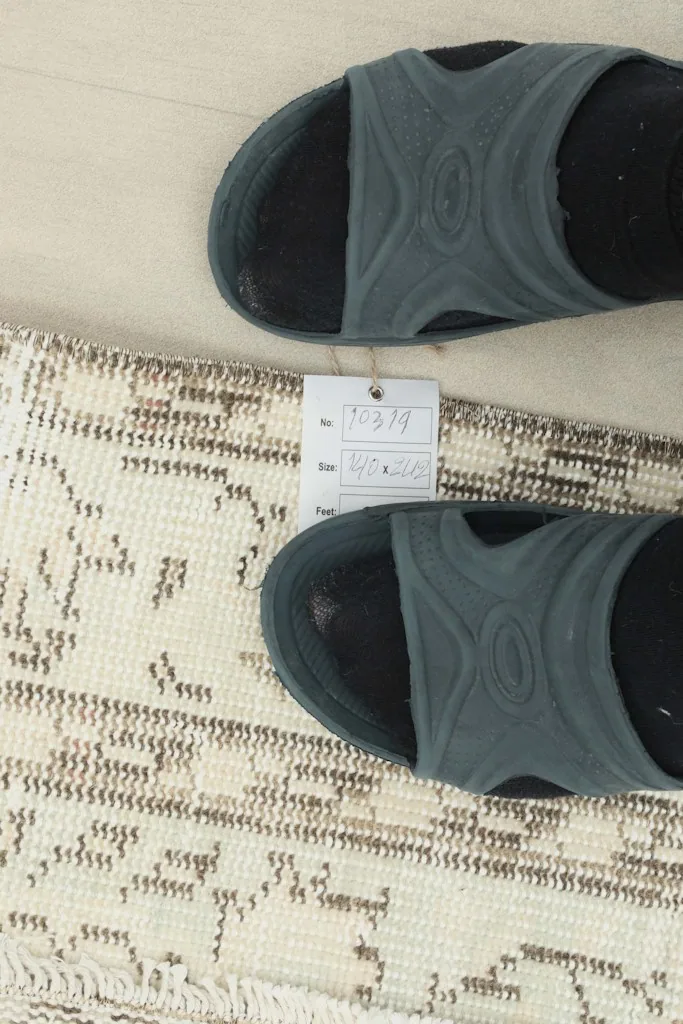 A pair of feet with slippers next to a tag, providing a sense of scale and the rug's texture.