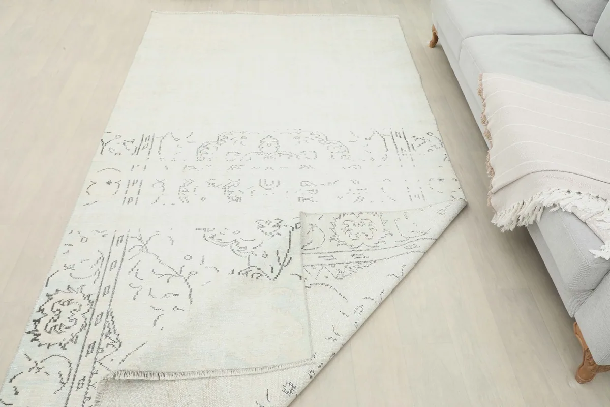 The ivory and gray rug partially rolled in a room setting next to a sofa