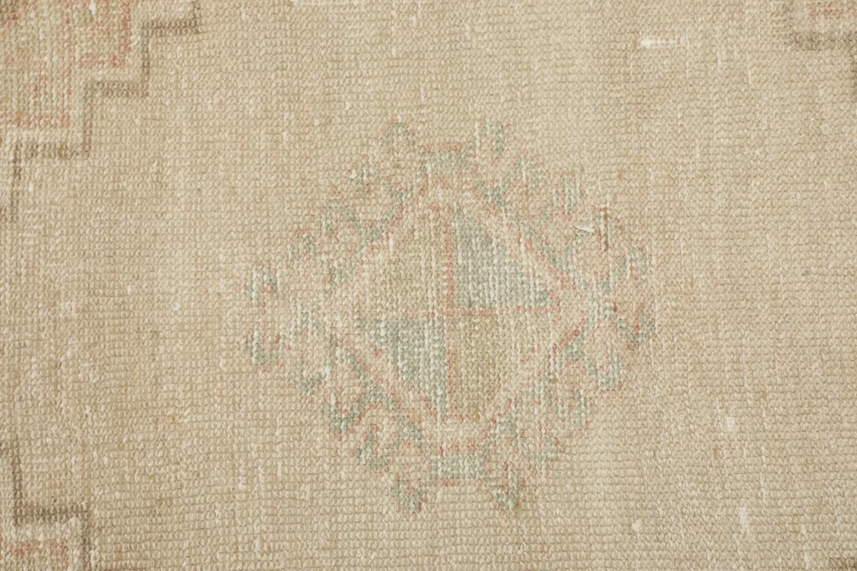 Close-up of the wool pile, revealing the faded rust and green hues within the geometric design.