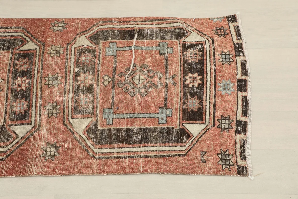 Close-up of one end of the runner, highlighting the rust field and charcoal geometric medallion with light beige accents.