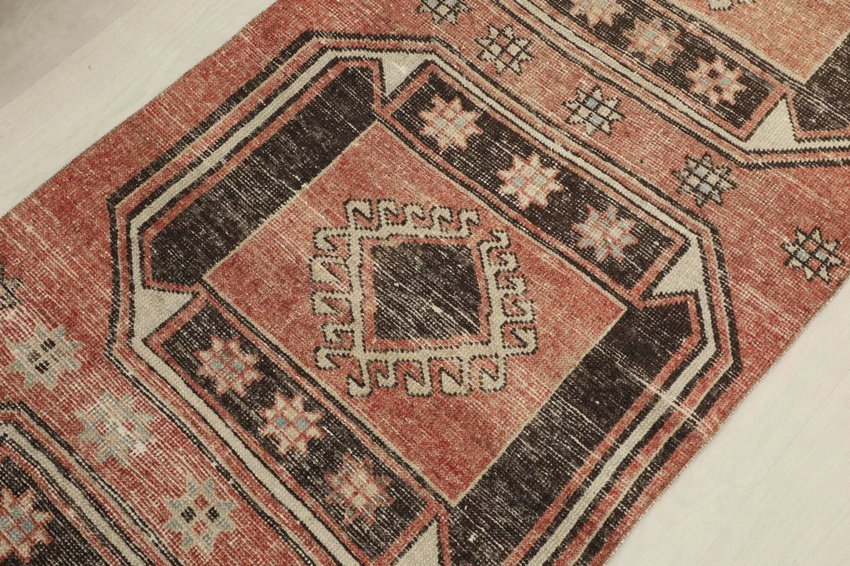 Angled close-up of a geometric medallion, revealing the faded rust and charcoal tones and subtle design variations.