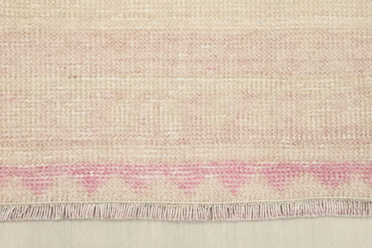 Close-up of the rug's end with soft pink fringes and a geometric border pattern