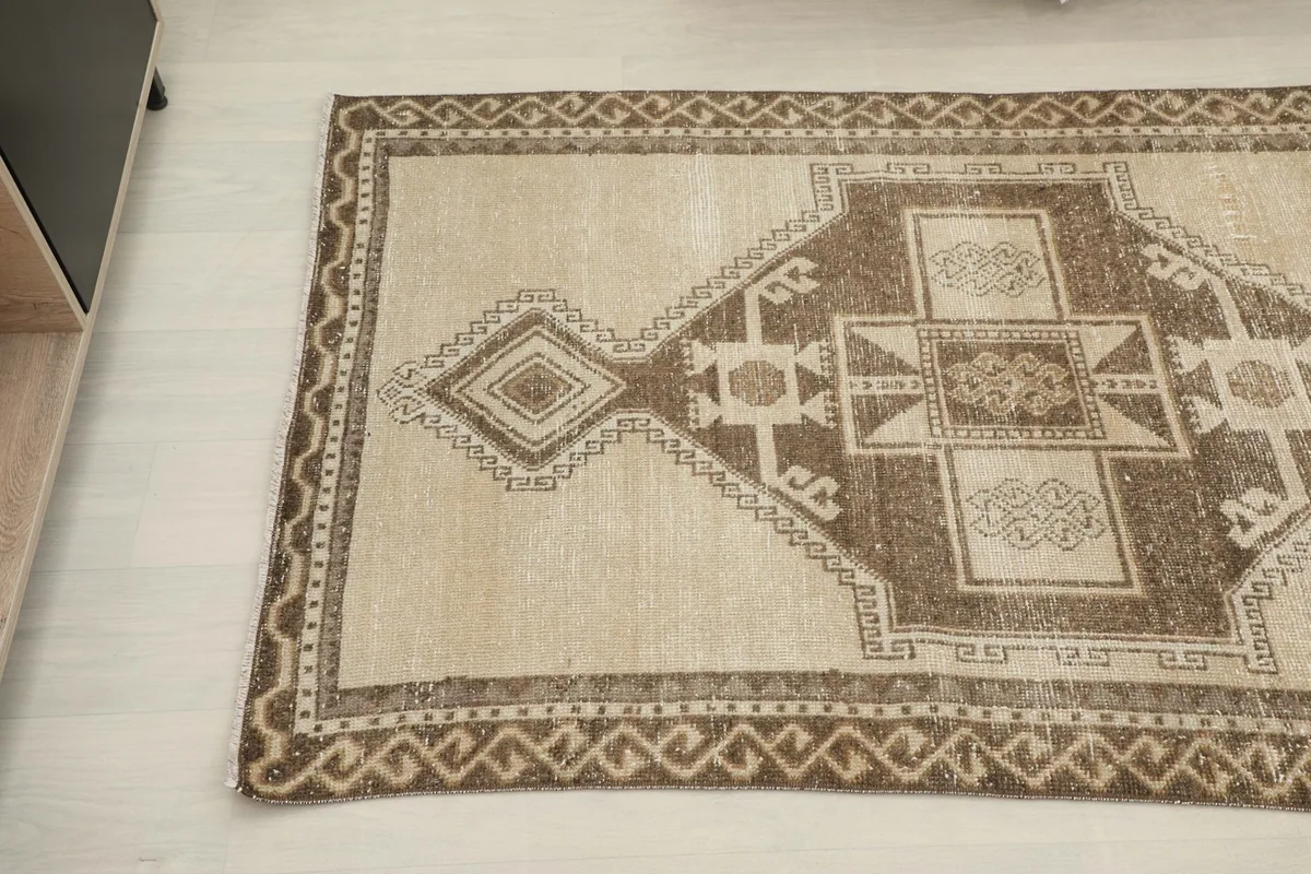 Partial view of the runner rug, focusing on the intricate border and central brown patterns.
