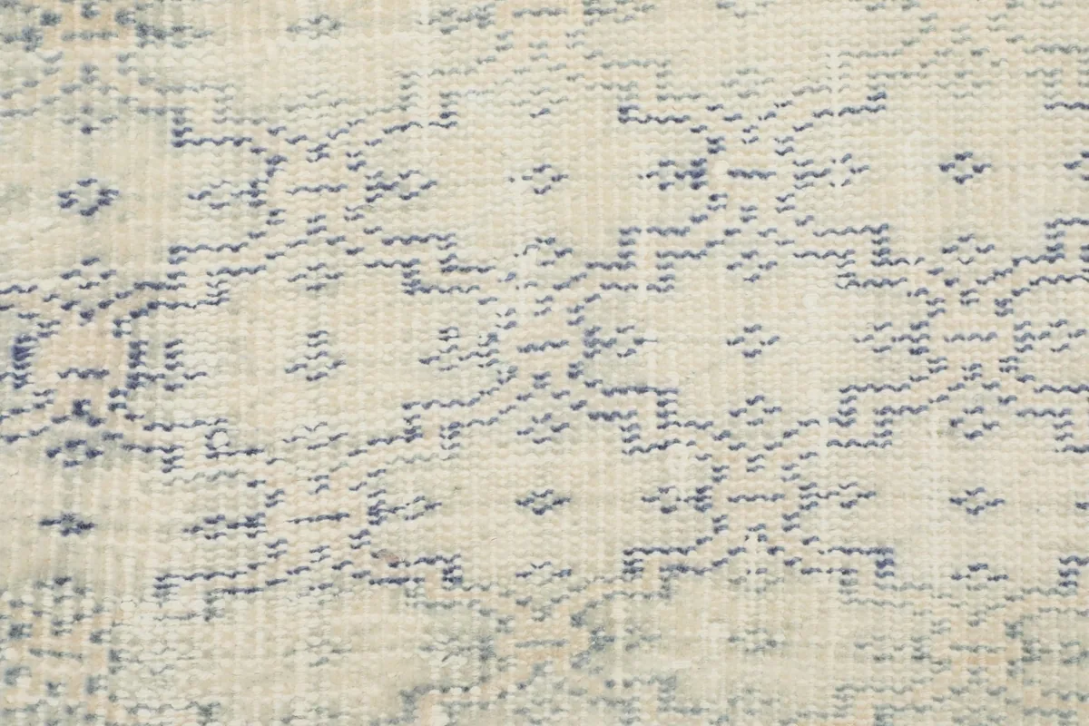Detailed view of the hand-knotted texture and faded blue patterns on the ivory field