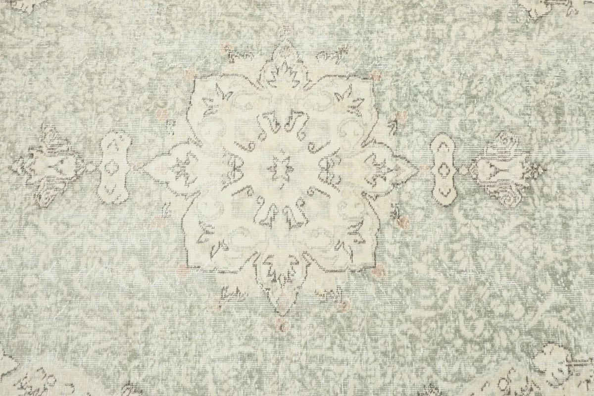 Detailed close-up of the central cream medallion and surrounding faded green field with motifs.