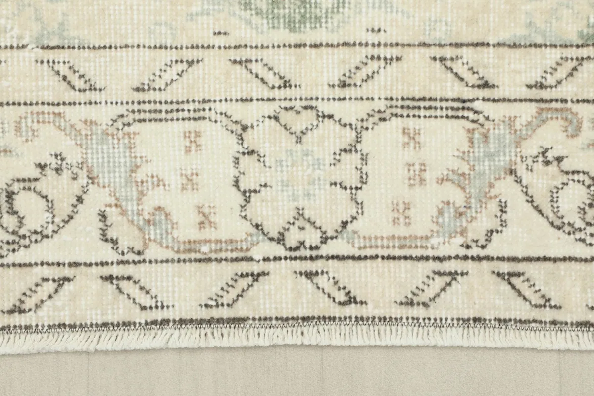 Detailed view of the rug's border, showcasing the intricate patterns in cream, tan, and beige tones.
