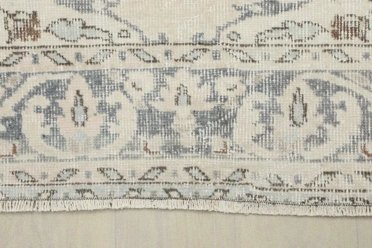 Close-up of the rug's border, revealing the faded gray and ivory patterns and fringe.