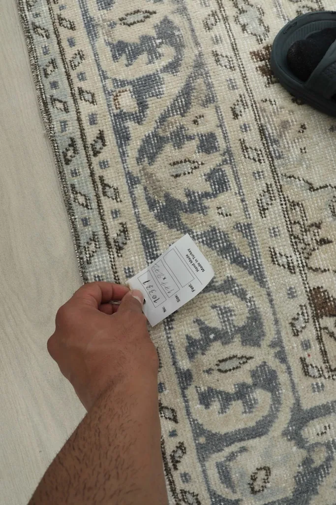 Hand holding a label over the back of the rug, showing the hand-knotted construction.