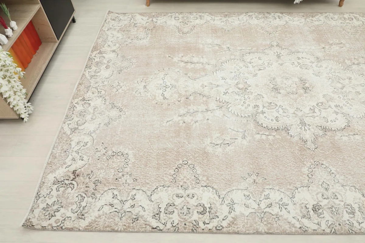 Another angled view of the large vintage rug, showing the blend of tan and ivory colors and distressed areas