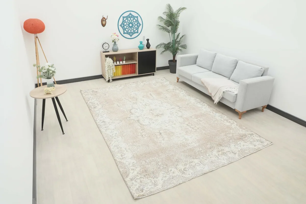 Large tan and ivory vintage rug placed in a modern living room setting with a light gray sofa