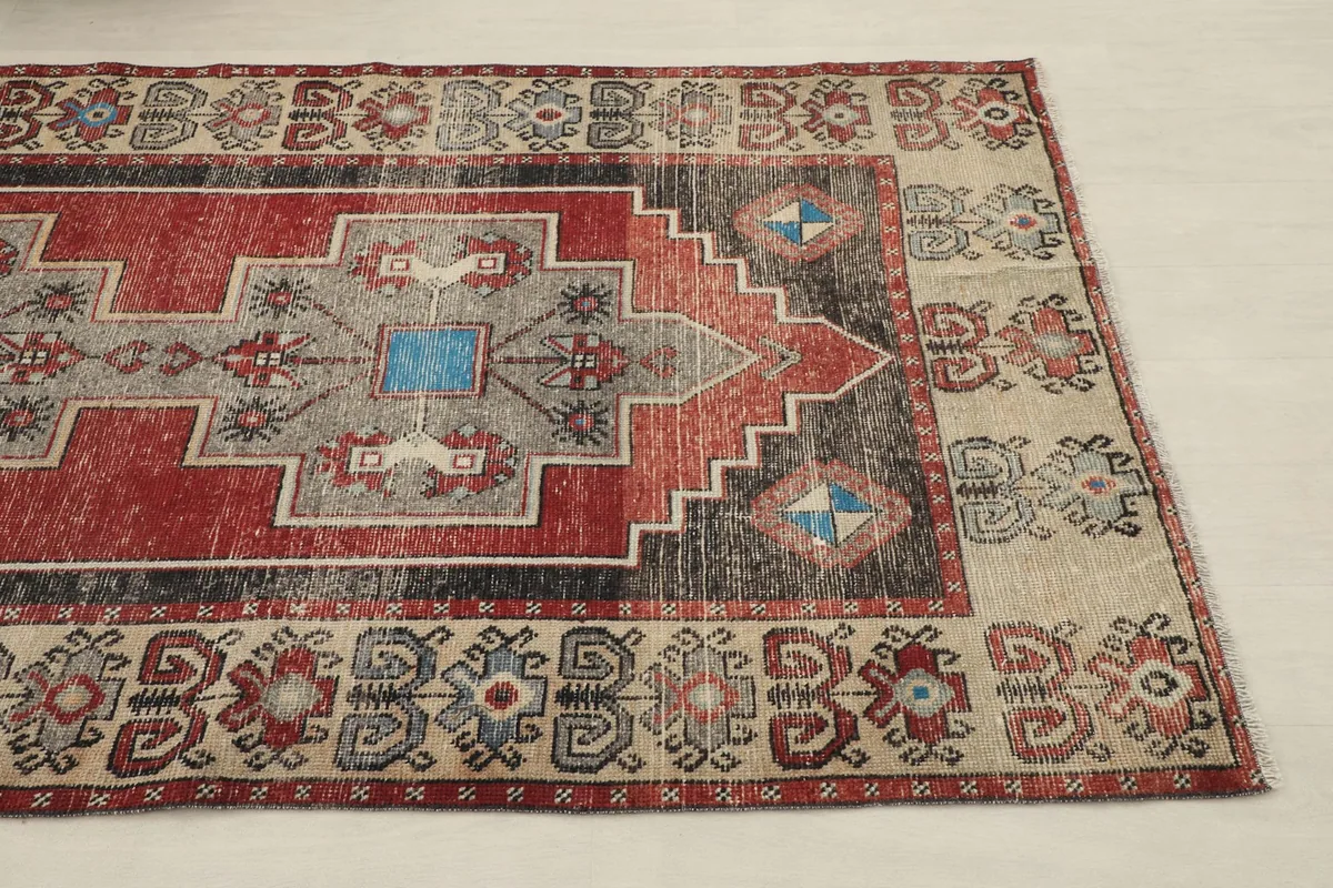 Angled view of the rug's design, showing the red field, gray center, and beige border patterns