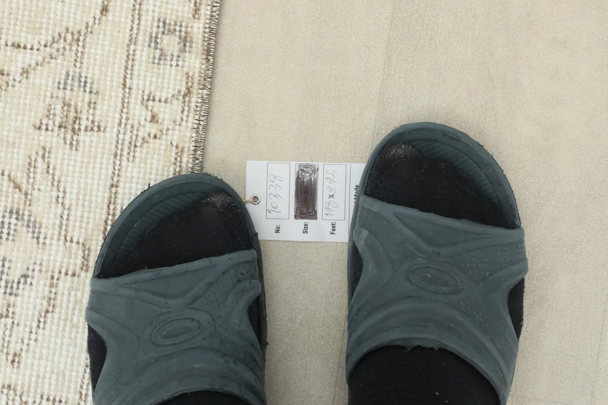 Feet in sandals next to a size reference card on the rug to show scale