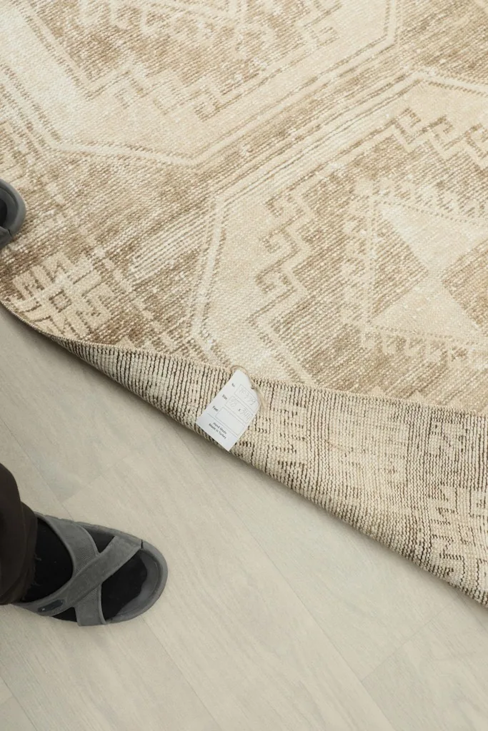 A person's feet next to the rug, showing its scale and the hand-knotted tag on the back