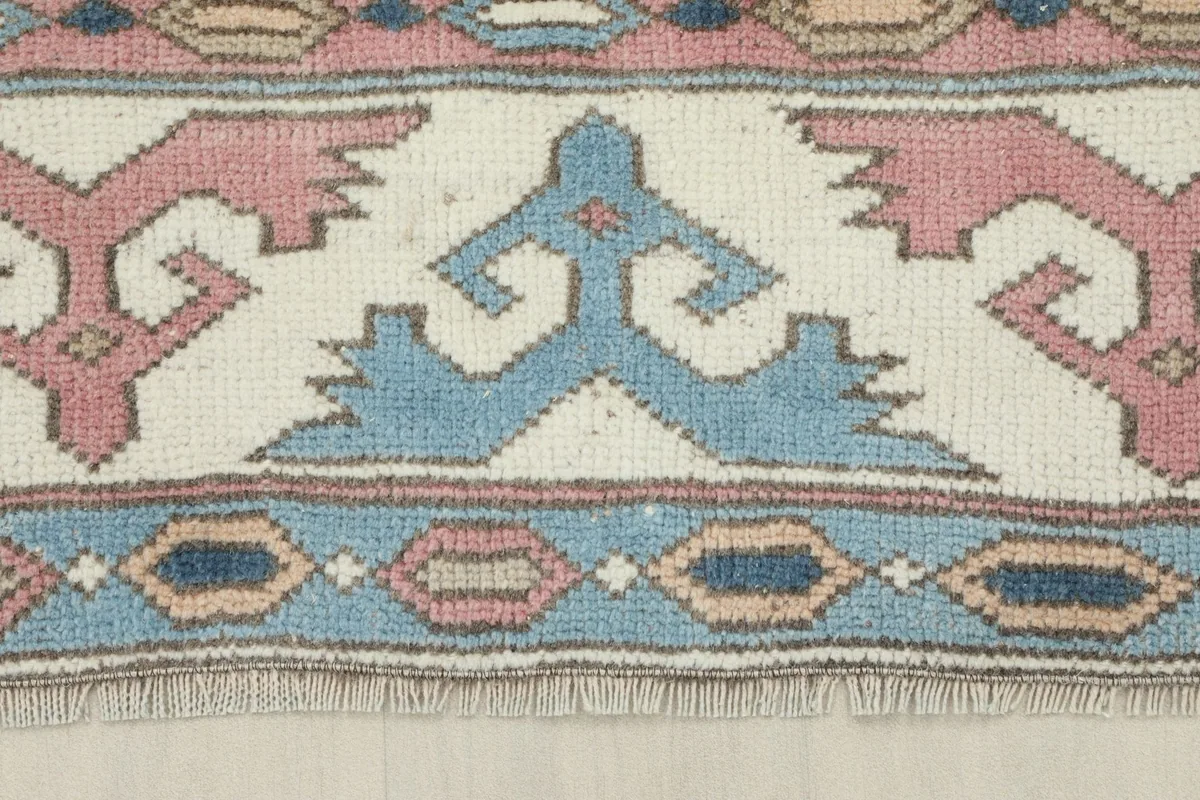 Detailed view of the ivory border with blue and rose geometric shapes and fringe