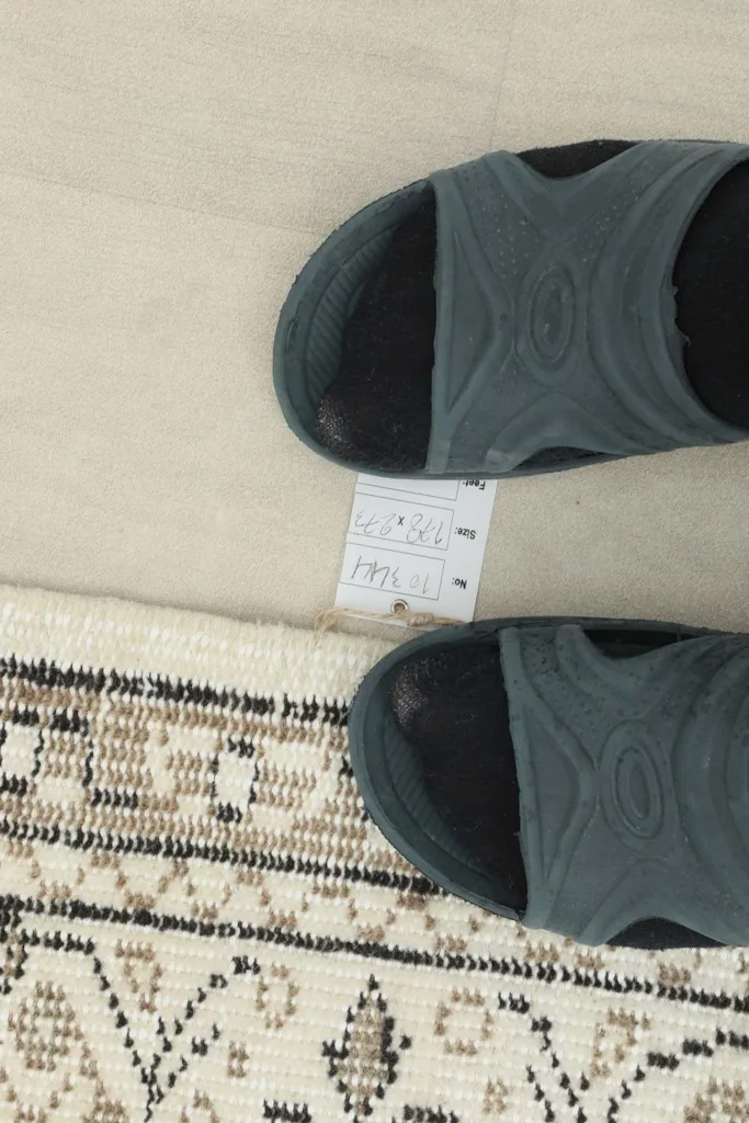 Measurement tag near the rug's edge, indicating the size in centimeters and inches next to sandals for scale