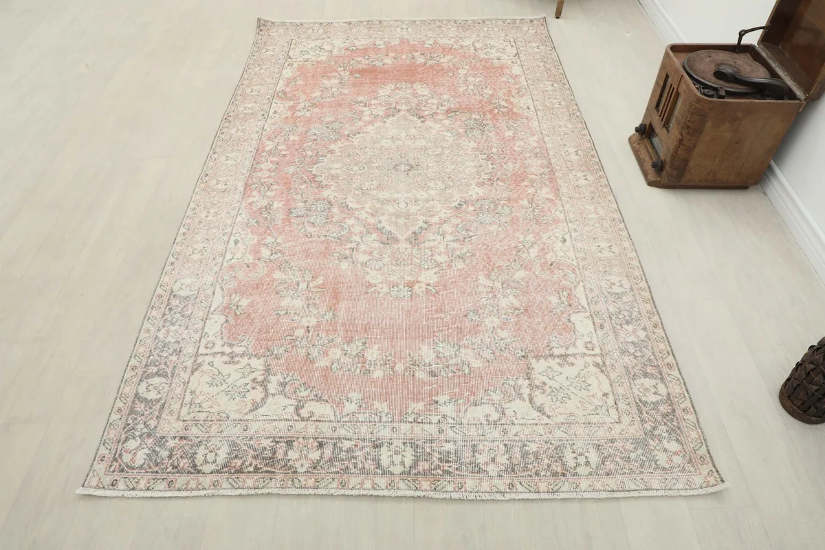 Vintage rose area rug displayed in a room setting with a wooden cabinet and chair