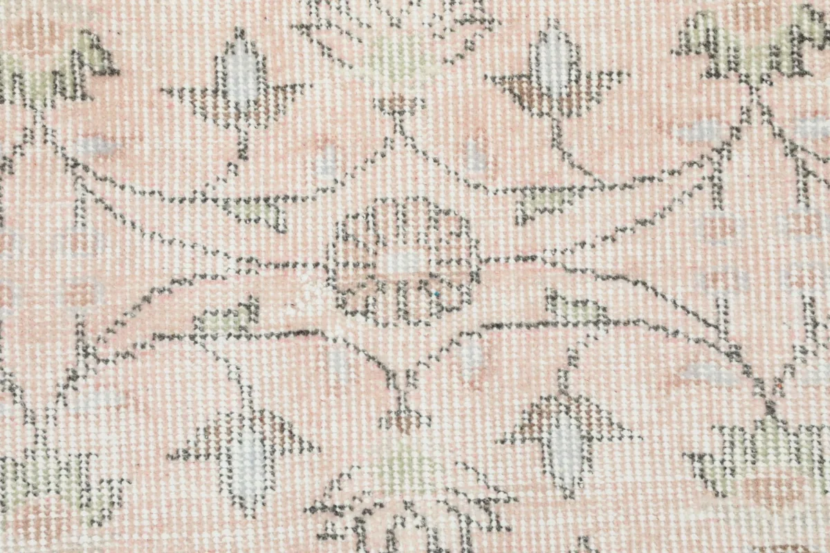 Detail of the low wool pile and hand-knotted floral motifs in rose and gray