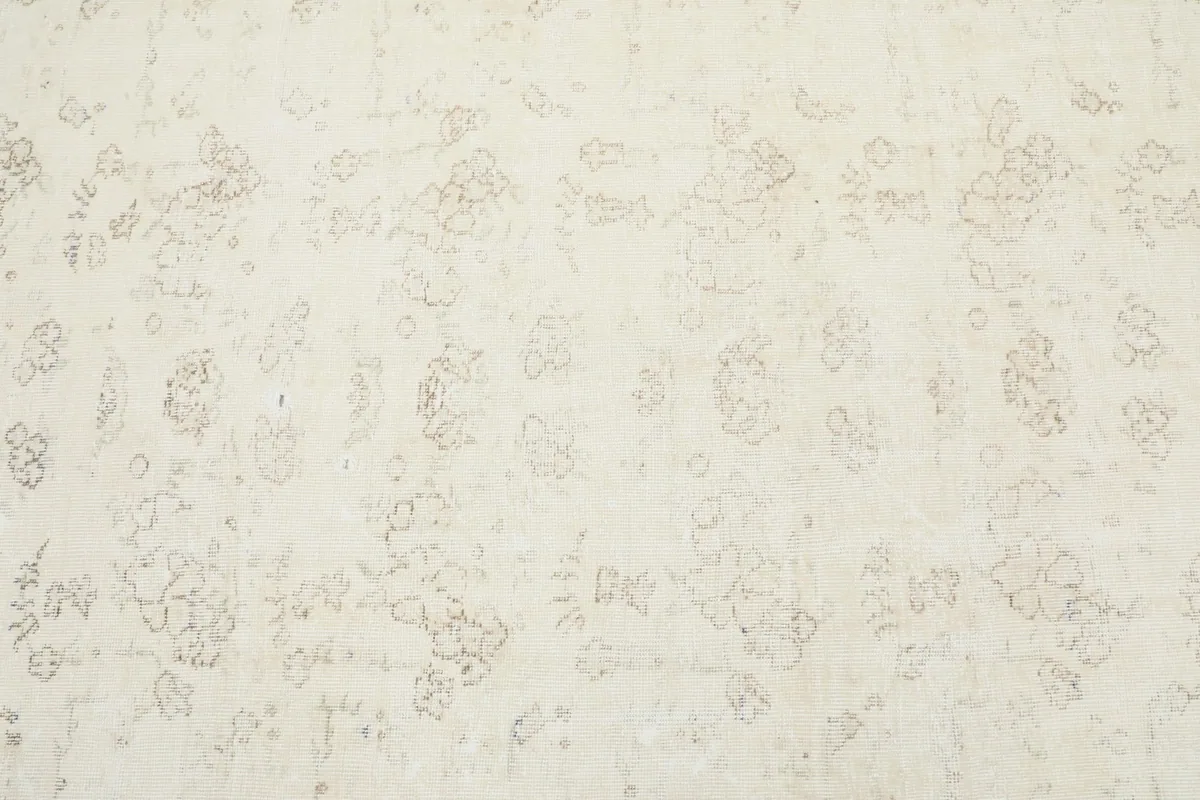 Detailed overhead shot of the rug's faded floral and geometric motifs in ivory and beige