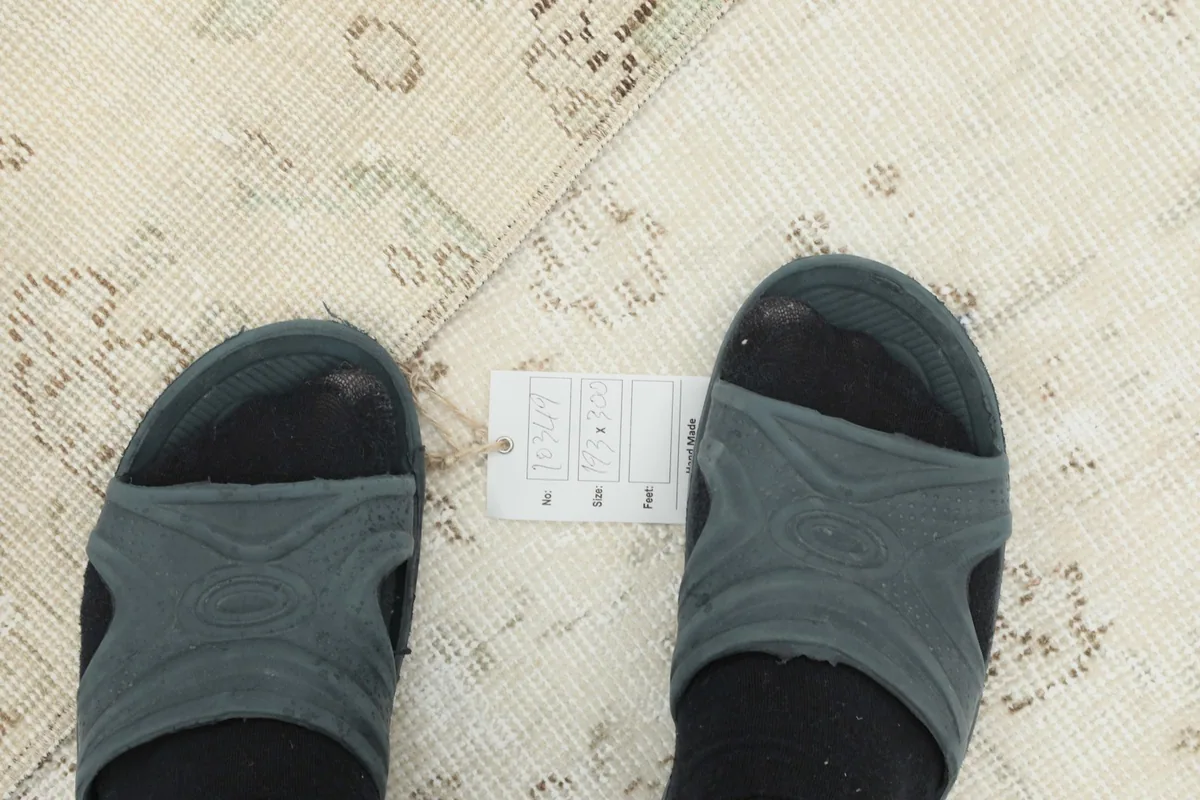 Feet in sandals next to a size tag on the rug, showing scale and texture