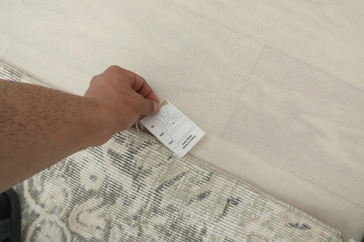 Hand holding a tag near the rug, indicating its quality and origin