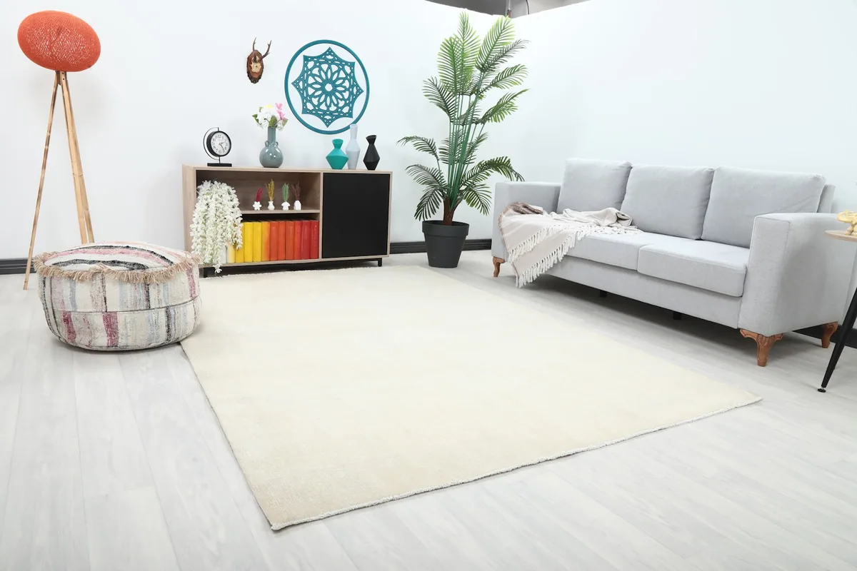 Angle view of the cream area rug placed in a living room, showing its scale with a sofa and decor.