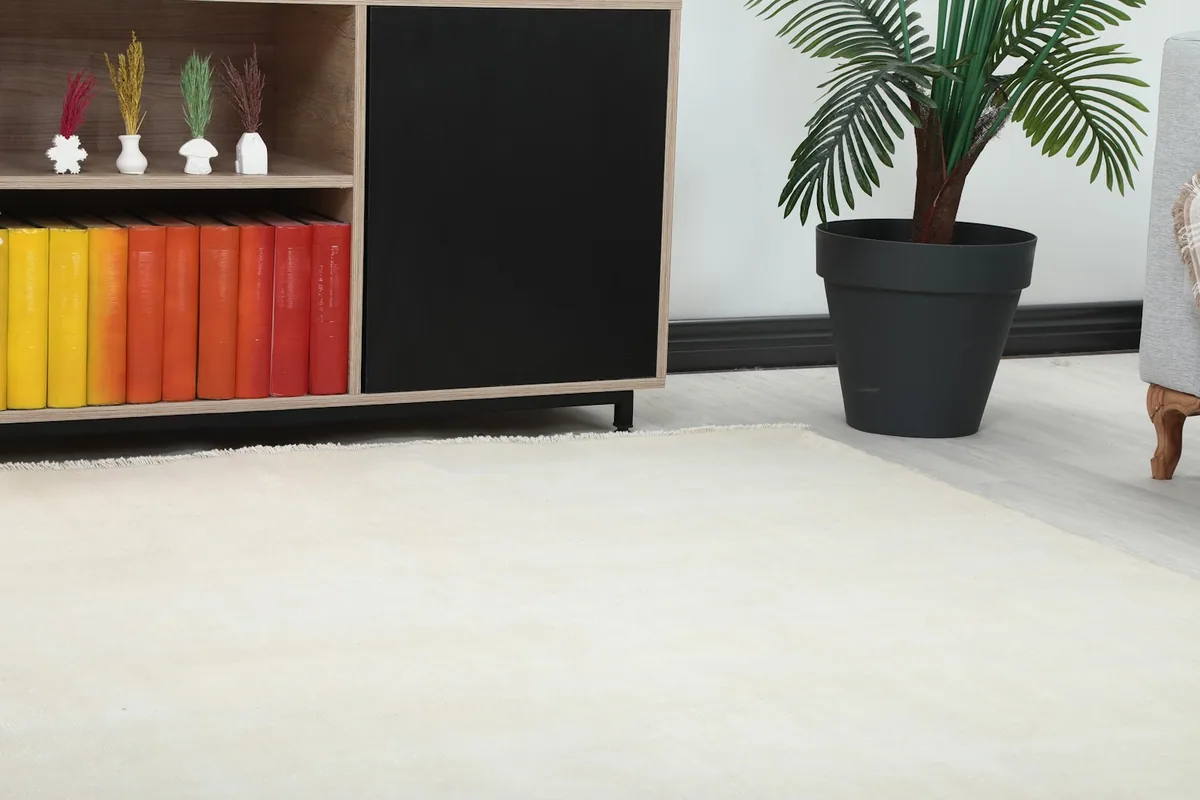 Close-up of the cream rug's texture and subtle color variations next to a wooden cabinet.