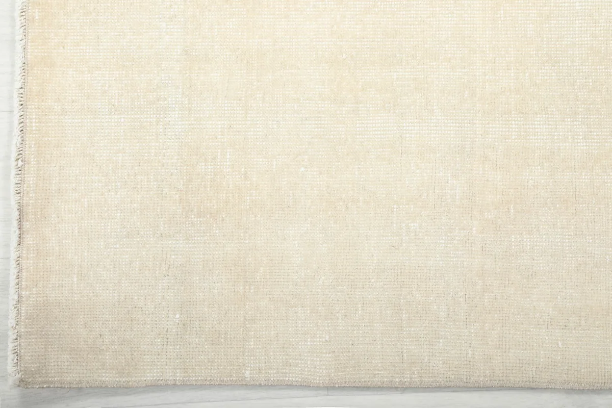Edge view of the cream rug, showing the finished border and short fringe.