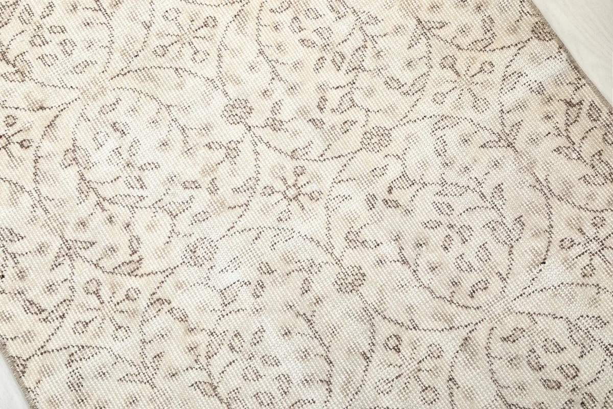 Close-up detail of the hand-knotted wool pile and intricate tan floral pattern on a cream background.