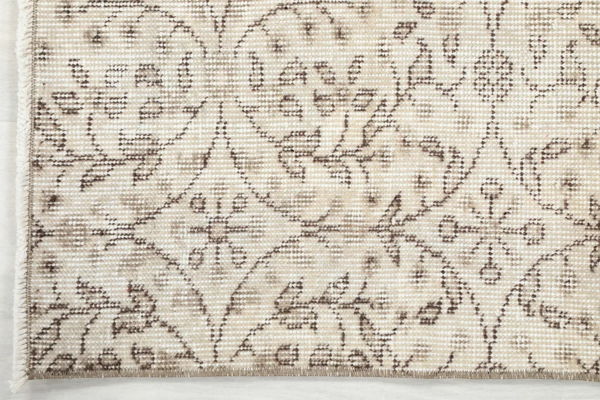 Detailed view of the rug's edge, showing the subtle color variations and wear on the tan motifs.