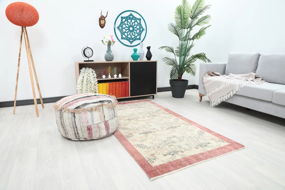Angle view of the ivory and rose rug in a living room, showing its placement next to a striped pouf