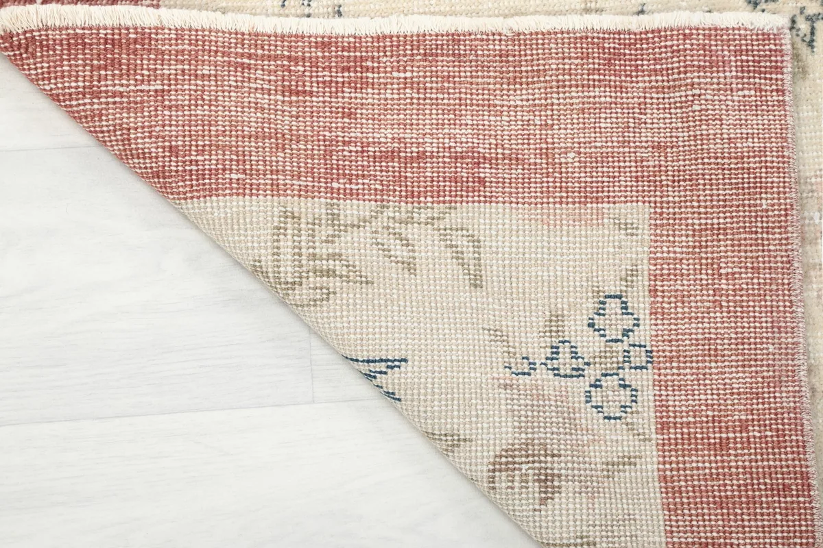 Underside of the rug with a corner folded back, showing the hand-knotted cotton foundation
