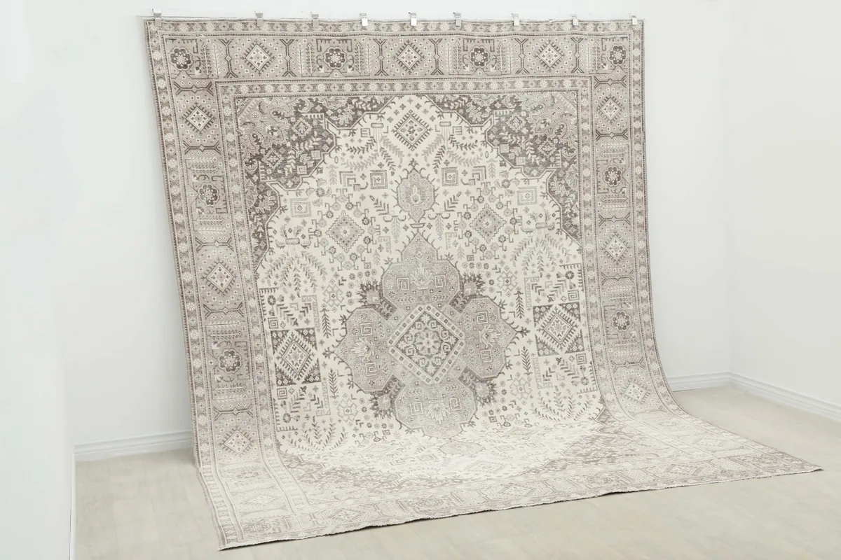Angled view of the large rug hung vertically, displaying its grand scale and intricate patterns