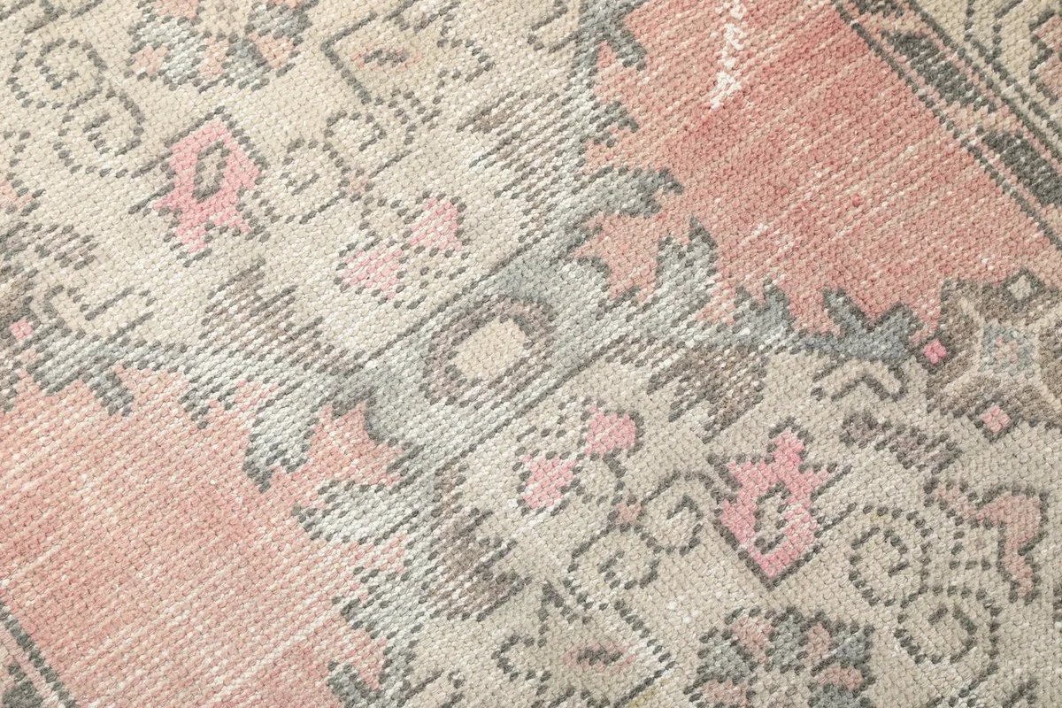 Detailed view of the rug's wool pile and hand-knotted texture with faded rose and gray colors